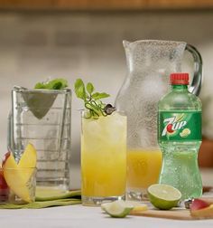 the pitcher is next to two glasses with lemonade, lime and apple slices in them