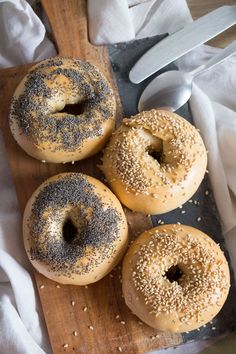 three bagels with sesame seeds on a cutting board next to a knife and napkin