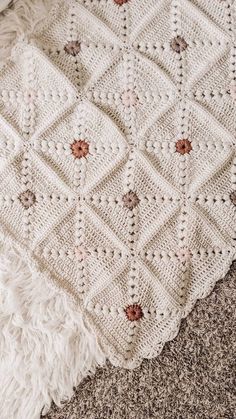 a white crocheted blanket sitting on top of a floor next to a rug