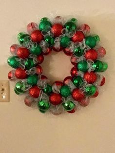 a christmas wreath with red and green ornaments hanging on the wall next to a light switch