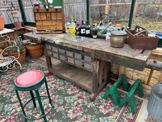 an old wooden table with lots of bottles on it and two stools next to it