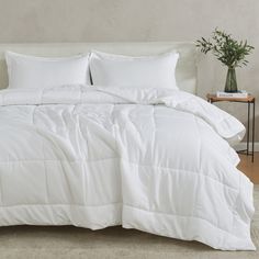 a bed with white comforter and pillows in a room next to a small table