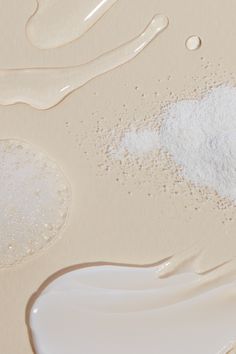 several different types of white powder on a beige surface with water droplets and sand bubbles