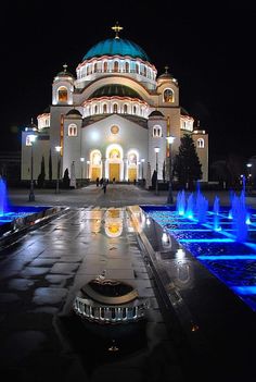 a large building with fountains in front of it and lights on the sides at night