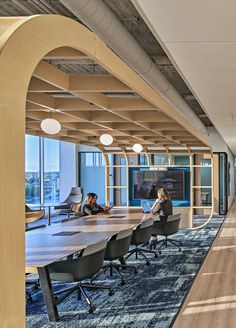 two people sitting at a conference table in an office with large windows and wooden columns