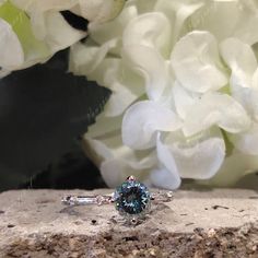 a blue diamond ring sitting on top of a stone wall next to white hydrangeas