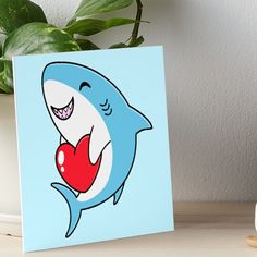 a cartoon shark with a heart in its mouth art board print on a table next to a potted plant