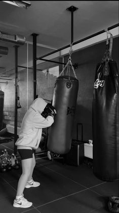 a woman in white shirt and black shorts standing next to punching bag on floor with other boxing equipment