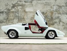 a white sports car parked in front of a concrete wall with its doors open and the door opened