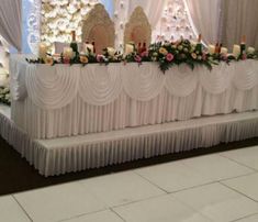 a table with candles and flowers on it in front of a wall decorated with white drapes