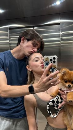 a man holding a small dog in front of a woman taking a selfie with her cell phone