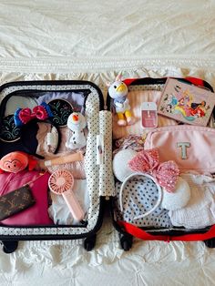 two pieces of luggage sitting on top of a white bed covered in clothing and accessories