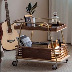 a guitar and some books on a cart in a living room with a window behind it