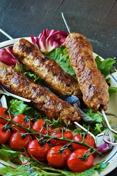 a plate with kebabs, tomatoes and lettuce