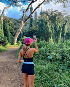 a woman standing on a dirt road taking a photo with her cell phone in the jungle