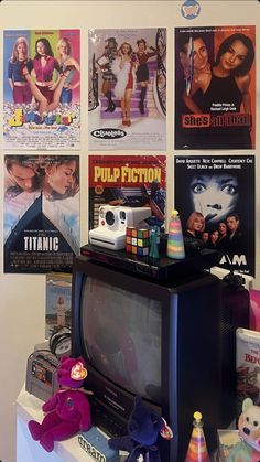 an old tv sitting on top of a dresser next to posters and toys in front of it