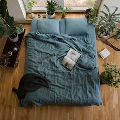 an overhead view of a bed with blue sheets and pillows, potted plants on the floor