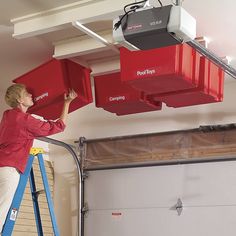 a woman on a ladder holding two red boxes in front of her head and another box above her head