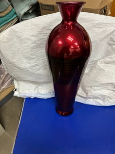 a large red vase sitting on top of a blue tablecloth covered floor next to a cardboard box