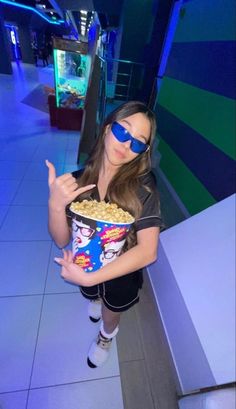 a girl wearing sunglasses and holding a bowl of popcorn