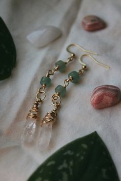 some green glass beads and gold earwires on a white cloth next to shells