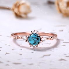 a turquoise stone and diamond ring sitting on top of a white table next to flowers