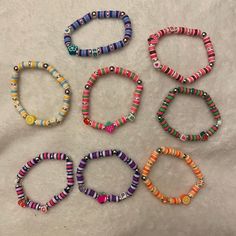 six bracelets with colorful beads are arranged on a white surface and one is empty