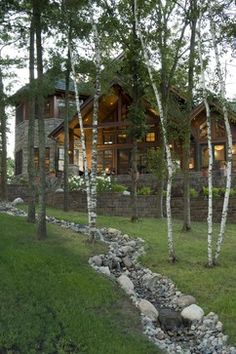 a house in the woods with trees and rocks on the ground next to it is surrounded by green grass