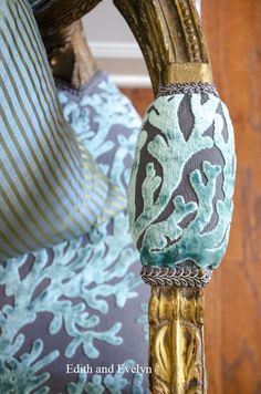 a close up of a gold and blue chair with pillows on the armrests