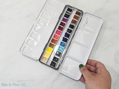 a person is holding a watercolor palette in their hand