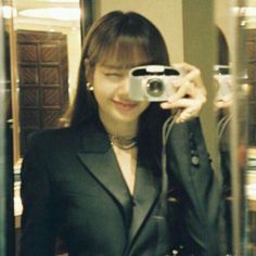 a woman taking a selfie in front of a mirror while wearing a black suit