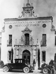 an old black and white photo of people standing in front of a building with cars parked outside