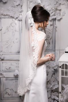 a woman in a white wedding dress with a veil on her head, standing next to a wall