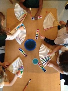 four children sitting at a table with paper fans and paintbrushes in front of them