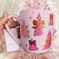 a hand holding a pink coffee mug with christmas trees on it and a gift tag