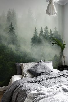 a bed sitting under a window next to a green forest wall mural on the side of a bedroom