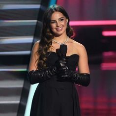 a woman in a black dress holding a microphone and smiling at the camera while standing on stage