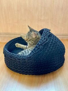 a cat laying in a blue knitted bed on top of a hard wood floor