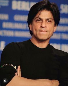 a man with his arms crossed posing for a photo in front of a blue background