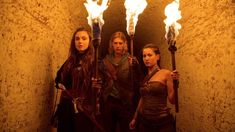 three people holding torches standing in front of a wall