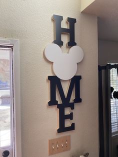 a mickey mouse sign mounted to the side of a wall next to a clock that says h is for me