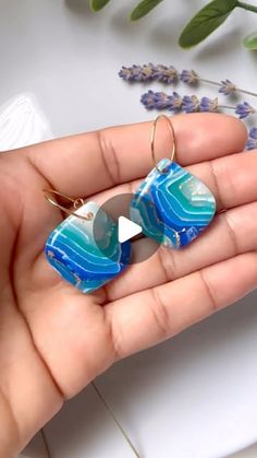 a hand holding a pair of earrings with blue and white designs on it, in front of flowers