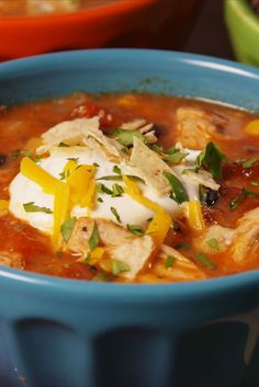 a blue bowl filled with chicken tortilla soup and sour cream cheese on top