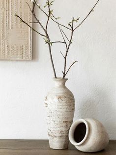 a white vase sitting on top of a wooden table next to a tree branch in it