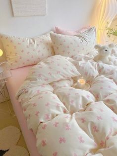 a bed with white and pink sheets, pillows and a teddy bear sitting on it