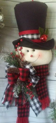 a snowman ornament hanging on the side of a building with pine cones and berries