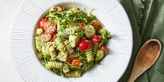 a white plate topped with pasta salad next to a wooden spoon and green napkins