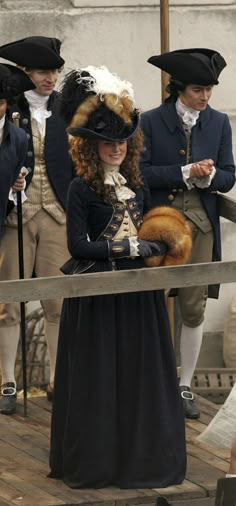 several people dressed in period clothing standing on a wooden platform and looking at something off to the side