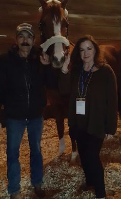 a man and woman standing next to a horse in a barn with hay on the ground