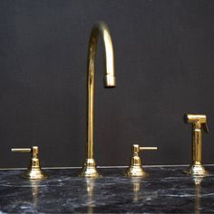 three brass faucets on a marble counter top